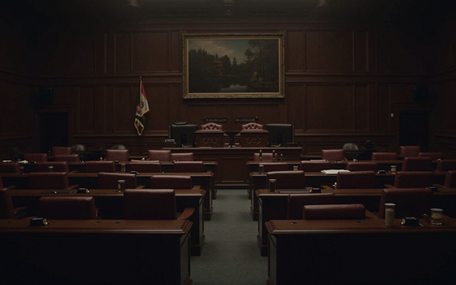 Empty legislative chamber with rows of wooden desks facing a raised dais