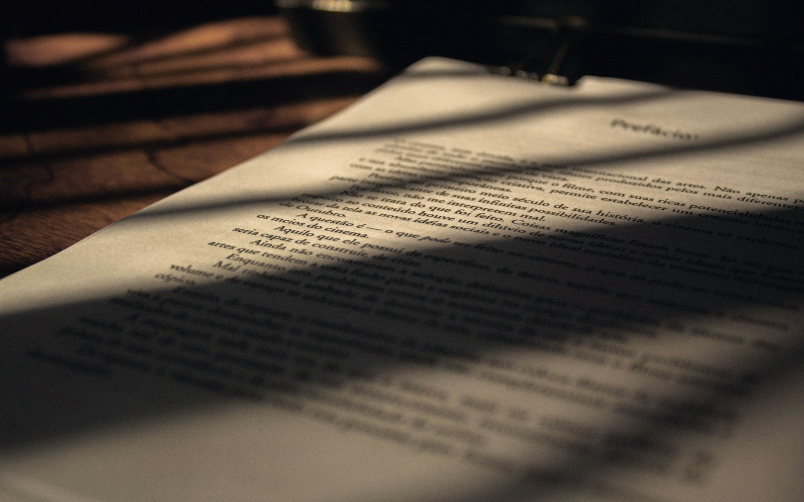 Shadows fall across a printed page of Portuguese text on a wooden desk